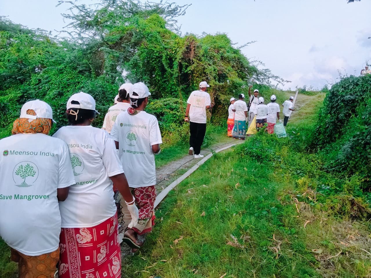 Residents in Meensou India shirts walking a path through coastal vegetation